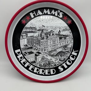 May include: Round metal tray with a red rim, white interior, and a black center. The center features a detailed black and white illustration of a building and the text "HAMM'S PREFERRED STOCK". Two red stars flank the word "HAMM'S".
