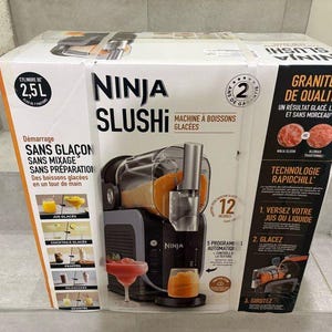 May include: A Ninja Slushi machine box with text in English and French. The box features a picture of the machine and images of slushies. The box also has a 2-year warranty and a 2.5L capacity.