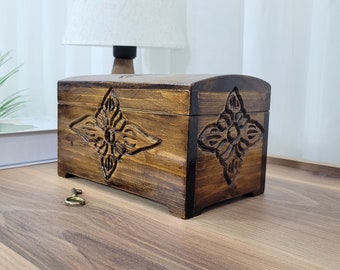 May include: A dark brown wooden box with intricate carved floral designs on the front and sides. The box has a hinged lid and a keyhole.