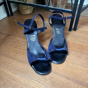 May include: A pair of navy blue suede sandals with an open toe, a thin ankle strap with a gold-tone buckle, and a black insole. The insole features the text Rangoni MADE IN FLORENCE Italy. A ribbed blue detail sits across the front of each shoe.