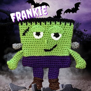 May include: A handmade crochet Frankenstein's monster doll named "FRANKIE". The doll is green, purple, and brown, with black stitches and a black hairline. The background features a full moon and bats. A Halloween-themed item.
