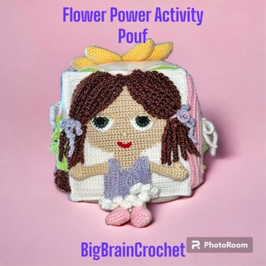 May include: A crocheted flower power activity pouf with a girl's face on one side. The pouf is made of different colored squares and has a yellow flower on top.