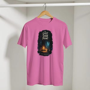 Könnte beinhalten: Rosafarbenes T-Shirt mit einem Grafikdesign, das den Text "THE LAST SAVE POINT" über einer Illustration einer Lagerfeuerszene in einem dunklen Wald zeigt. Der Text "BEFORE THE FINAL BOSS" steht darunter.