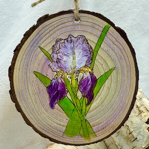 May include: A purple and green iris flower painted on a round wooden slice with a twine hanger.