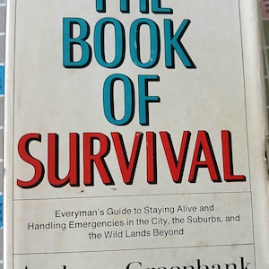 May include: A vintage book titled "THE BOOK OF SURVIVAL" with teal and red lettering on a cream-colored cover. The book's subtitle reads "Everyman's Guide to Staying Alive..." by Anthony Greenbank. The book is placed on a Scrabble board.
