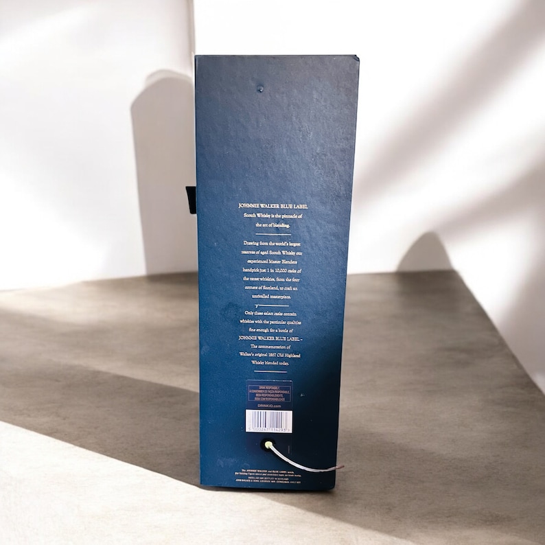 Op de afbeelding: Een blauwe kartonnen doos met gouden letters die "JOHNNIE WALKER BLUE LABEL" lezen en de Schotse whisky beschrijven als de top van de kunst van het blenden. De doos vermeldt ook dat alleen de beste vaten voor deze whisky worden geselecteerd.