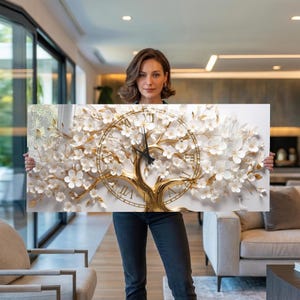 May include: A rectangular wall clock featuring a gold tree design with white flowers and a clock face. The clock has Roman numerals and black clock hands. The clock is held by a person.
