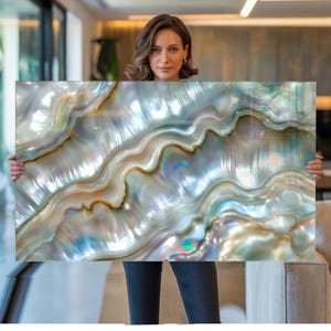 Può includere: Un'opera d'arte murale rettangolare con una finitura in madreperla iridescente ad alta lucentezza. La superficie presenta motivi a onde organiche e fluide in tonalità crema, oro tenue, azzurro pallido e argento, creando un effetto scintillante.