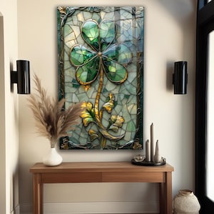 May include: A framed stained glass artwork featuring a large green shamrock with gold accents. The artwork is set against a mosaic background of green and white tiles, with a decorative gold border. The artwork is displayed above a wooden console table.
