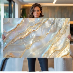 Könnte beinhalten: Ein rechteckiges Wandkunstwerk mit einer perlmuttartigen, irisierenden weißen Oberfläche und fließenden, wellenförmigen Texturen. Das Design wird durch dünne, organische Goldlinien akzentuiert, die den Wellen folgen und einen Schichteffekt erzeugen.