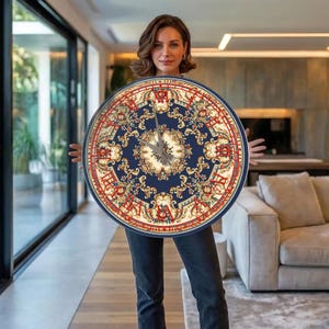 Könnte beinhalten: Runde Wanduhr mit marineblauem Zifferblatt mit detailliertem Blumendesign und roten römischen Ziffern. Die Uhr hat einen roten Außenring und goldfarbene Akzente. Die Zeiger sind silberfarben.