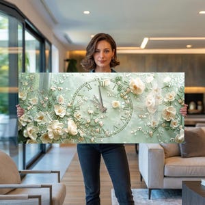 Könnte beinhalten: Ein rechteckiges Wandkunstwerk mit einem Zifferblatt-Design mit römischen Ziffern und floralen Verzierungen. Die Uhrzeiger sind silberfarben und der Hintergrund ist ein sanftes Grün. Weiße und cremefarbene Blumen sind um das Zifferblatt angeordnet.