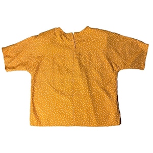 May include: A short-sleeved, yellow shirt with a white polka dot pattern. The shirt has a round neckline and a button closure in the back.