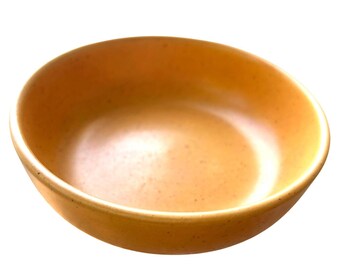 May include: A round, light orange ceramic bowl with a speckled texture. The bowl has a smooth interior and a slightly raised rim. The bowl is empty and sits against a white background. The bowl is suitable for serving food.