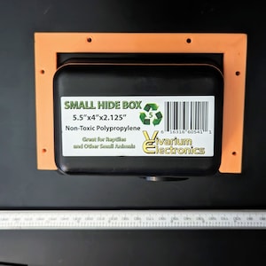 May include: A small black hide box for reptiles and other small animals. The box is made of non-toxic polypropylene and measures 5.5 inches by 4 inches by 2.125 inches. The box is labeled "SMALL HIDE BOX" and has a barcode.