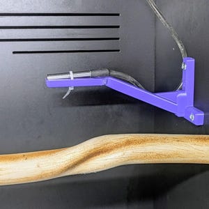 Könnte beinhalten: Eine violette L-förmige Montagehalterung, die mit zwei Schrauben an einer schwarzen Oberfläche befestigt ist. Eine silberne Metallsonde ist mit einem weißen Kabelbinder an der Halterung befestigt, und ein schwarzes Kabel führt von der Sonde weg.