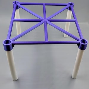 May include: A purple plastic square frame with a geometric design, supported by four white cylindrical legs.