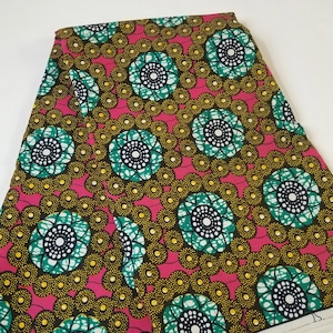 May include: A folded stack of pink and green fabric with a repeating pattern of large, stylized flowers. The flowers have a black center and are surrounded by a ring of small yellow dots.
