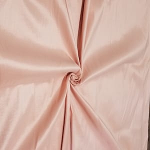 Puede incluir: Primer plano de una tela lisa de color rosa pálido con una textura suave y sedosa. La tela está doblada y drapeada, creando un suave patrón de ondas.