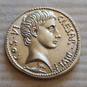 Peut inclure: Une pièce de monnaie dorée avec un profil d'homme d'un côté et un petit animal de l'autre. La pièce porte l'inscription "CAESAR" sur le bord.