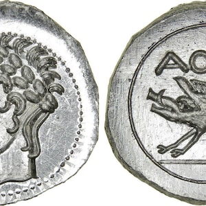 May include: A silver coin featuring a profile of a man with curly hair and a helmet on one side. The other side depicts a boar with the inscription "AOYE" above it. The coin has a circular shape with an irregular edge.