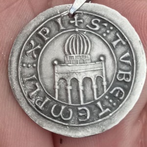 Pode incluir: Um pingente de prata com um design detalhado de um edif&iacute;cio com uma c&uacute;pula no topo. O pingente &eacute; inscrito com o texto "XPIST: STVB: E: M: PI".