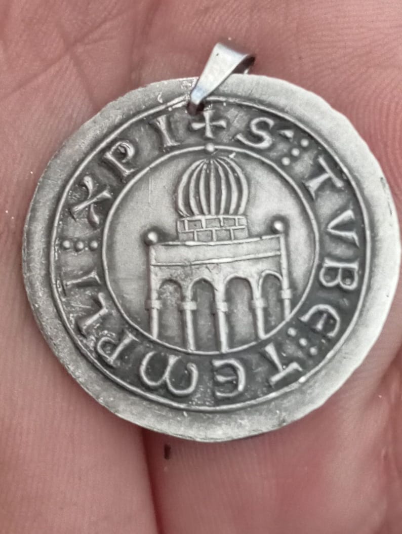 Pode incluir: Um pingente de prata com um design detalhado de um edif&iacute;cio com uma c&uacute;pula no topo. O pingente &eacute; inscrito com o texto "XPIST: STVB: E: M: PI".