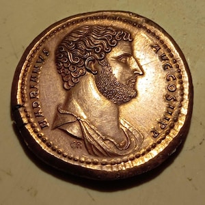 Puede incluir: Una moneda romana de bronce con la inscripción "IMP. HADRIANVS AVG COS III P.P." y un retrato del emperador romano Adriano en el anverso.