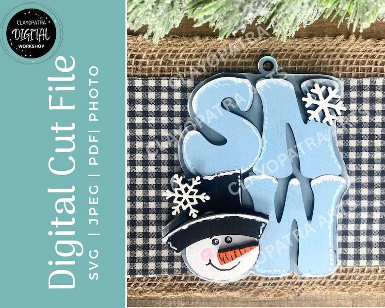 May include: A wooden snowman-themed ornament with the word "SNOW" in light blue letters. The snowman has a black hat, a carrot nose, and a smiling face. A snowflake is placed above the "W". The background includes a blue and white checkered pattern.
