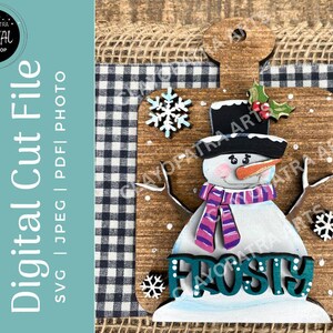 May include: A wooden snowman decoration with a black top hat, orange carrot nose, and a purple and pink scarf. The word "Frosty" is displayed in teal letters. The background includes a black and white checkered pattern and a burlap border.