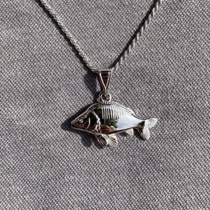 Peut inclure: Un collier en argent avec un pendentif en forme de poisson argenté détaillé. Le poisson est tourné vers la droite et a une surface texturée.