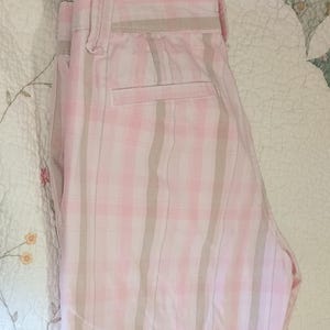 May include: Pink and white plaid pants with a light brown stripe design. The pants have a back pocket and a waistband with belt loops. The fabric appears to be cotton or a similar material.