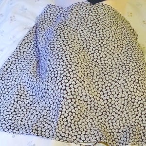 May include: A black and white floral print skirt. The skirt features a pattern of small white flowers on a black background. The fabric appears to be lightweight and flowing, with a slight sheen.