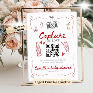 May include: A framed baby shower sign with the text "Capture the Love" in red script. The sign includes illustrations of a camera, baby bottle, and a soda bottle. The sign also includes a QR code and the text "Camille's baby shower 05/28/2030".