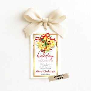 Può includere: Un'etichetta regalo bianca con bordo dorato e fiocco color crema. L'etichetta presenta la parola "holiday" in corsivo rosso, un'illustrazione ad acquerello di arance, bastoncini di cannella e bacche e il testo "Merry Christmas."