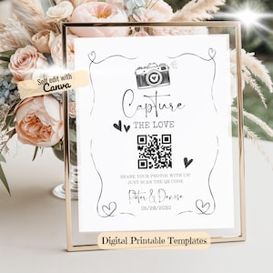May include: A framed wedding sign with the words "Capture the Love" and a QR code. The sign also includes the names "Peter & Denise" and the date "05/28/2030". The sign is in a gold frame and is surrounded by flowers.