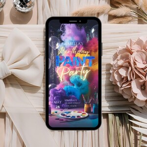 Op de afbeelding: Een kleurrijke digitale uitnodiging voor een verjaardags-verfparty. De uitnodiging toont een telefoonscherm met een achtergrond van kleurrijke rook en verfspatten. De tekst "Isabella's Birthday Paint Party" is geschreven in een neon-lettertype. De datum "May 28" staat in de linkerbenedenhoek. De uitnodiging bevat ook het adres en andere details.