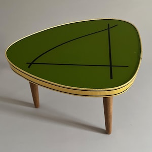 Könnte beinhalten: Ein Beistelltisch im Mid-Century-Modern-Stil mit einer grünen, tropfenförmigen Tischplatte. Die Tischplatte hat schwarze geometrische Linien und ist mit Gold und Schwarz eingefasst. Der Tisch hat drei Holzbeine.