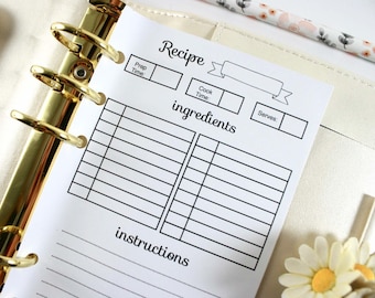 May include: A white recipe sheet with black text, held in a gold binder. The sheet includes sections for prep time, cook time, ingredients, and instructions. A floral pencil and a daisy are in the background.