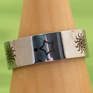 May include: A silver ring with a star and two sun designs engraved on it.