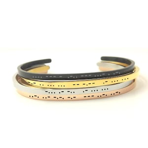 May include: Four stacked bracelets with a braille pattern. The bracelets are in black, gold, silver, and rose gold.