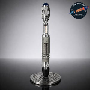 May include: A silver-colored prop with a blue top and a textured gray body, standing on a round, engraved base. The prop has a detailed design with a clear, yellow wire visible inside. The image includes a logo that says "SONIC CORPORATION" and "MAKER OF FINE REPLICAS AND PROPS."