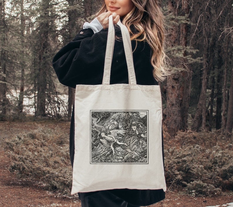 May include: A white canvas tote bag with black handles. The bag features a black and white illustration of a scene from a fantasy novel. The illustration depicts a group of fairies flying through a forest.