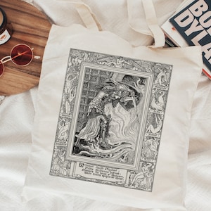 May include: A black and white tote bag with a vintage illustration of a knight in armor holding a sword. The illustration is surrounded by a decorative border with the words "Brightness doth Obscure: Shadows, the Substance of the Heart; Where Love's Splendour doth appear."