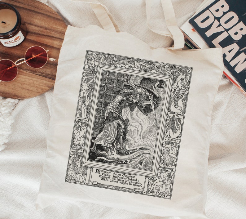 May include: A black and white tote bag with a vintage illustration of a knight in armor holding a sword. The illustration is surrounded by a decorative border with the words "Brightness doth Obscure: Shadows, the Substance of the Heart; Where Love's Splendour doth appear."
