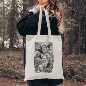 Pode incluir: Uma sacola tote creme com uma ilustração detalhada em preto e branco. A obra de arte retrata criaturas míticas e elementos arquitetônicos. A sacola tem alças resistentes para transportar.