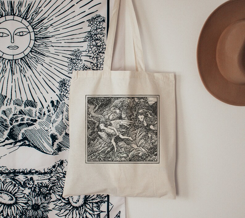 May include: A white canvas tote bag with black handles. The bag features a black and white illustration of a winged figure flying through a forest.