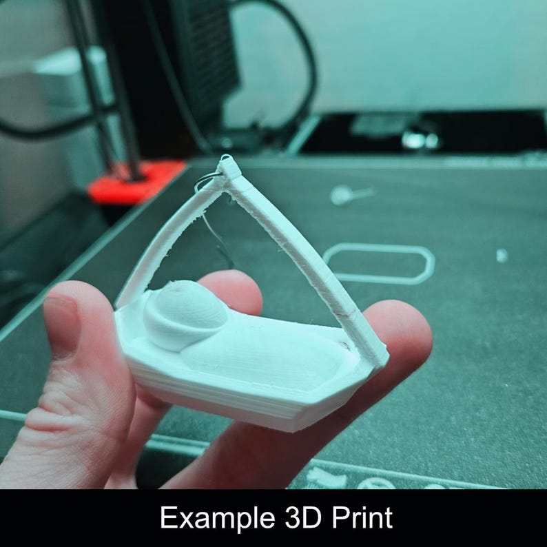 Puede incluir: Una figura blanca impresa en 3D que representa a un peque&ntilde;o personaje acostado en una cuna con un marco de dosel arqueado. El objeto tiene un acabado mate y liso, construido en una sola pieza con l&iacute;neas de capa visibles del proceso.