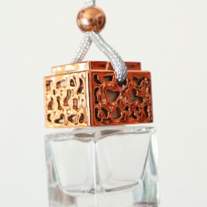 May include: A clear glass bottle with a rose gold metal top and a decorative design. The bottle is hanging from a gray string.