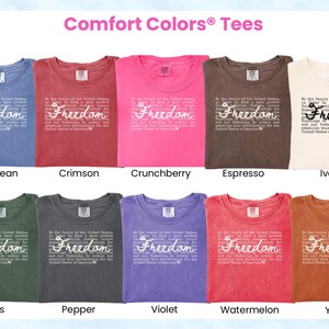 May include: A display of Comfort Colors tees in various colors, including blue jean, crimson, and ivory. Each shirt features the word "Freedom" in a cursive font, along with a quote. The shirts are arranged in rows, showcasing the range of available colors.